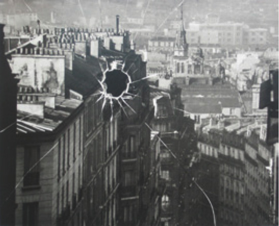 Schwarzweißfotografie: Blick über die Dächer von Paris, in der Bildmitte ein sternförmiges Loch mit Rissen, die zu den Rändern ausstrahlen.